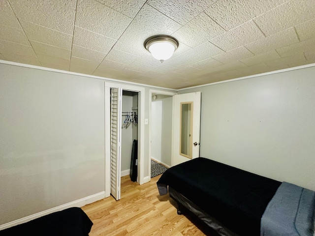 bedroom with light wood finished floors, ornamental molding, a closet, and baseboards
