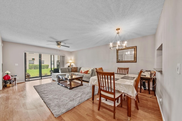 dining space with ceiling fan with notable chandelier, light wood-type flooring, and a textured ceiling