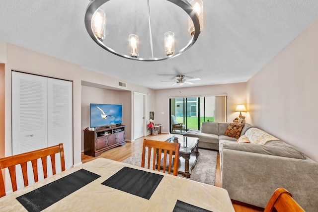 dining space featuring light hardwood / wood-style flooring, ceiling fan with notable chandelier, and a textured ceiling