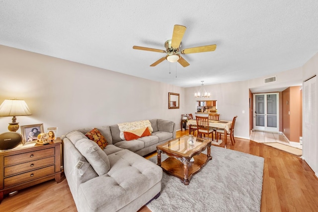 living room featuring ceiling fan with notable chandelier, light hardwood / wood-style floors, and a textured ceiling