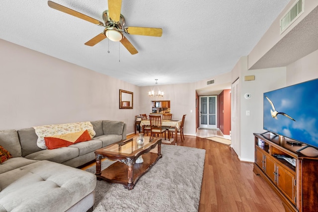 living room with ceiling fan with notable chandelier, wood-type flooring, and a textured ceiling