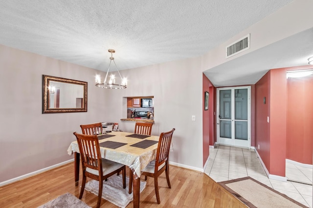 dining space with light hardwood / wood-style flooring, a textured ceiling, and an inviting chandelier