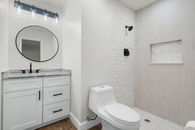 bathroom featuring toilet, hardwood / wood-style flooring, vanity, and a tile shower