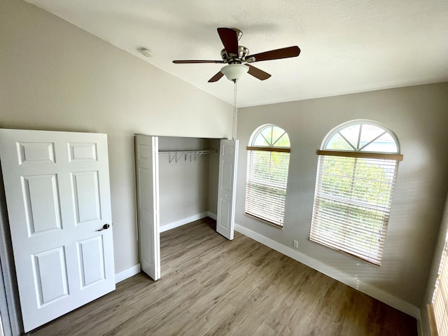 unfurnished bedroom with a closet, lofted ceiling, light wood-type flooring, and ceiling fan