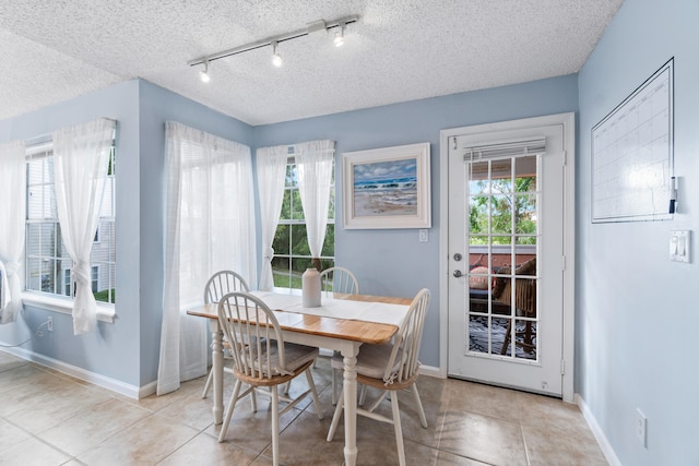 dining space with a textured ceiling, rail lighting, and light tile patterned floors