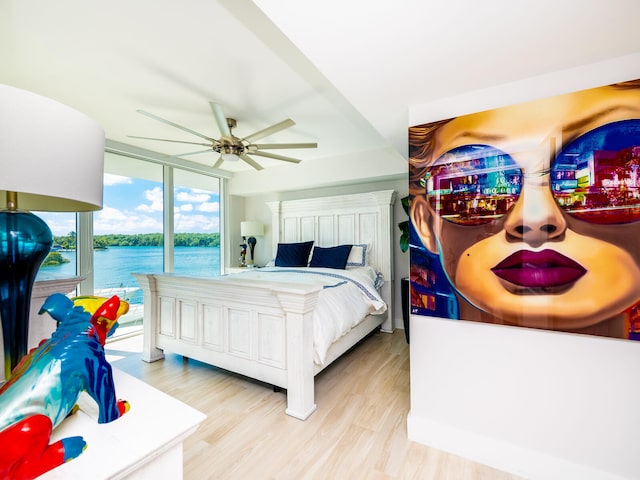 bedroom with light wood-type flooring, a water view, and ceiling fan