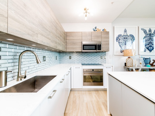 kitchen with white cabinetry, appliances with stainless steel finishes, decorative backsplash, sink, and light hardwood / wood-style flooring