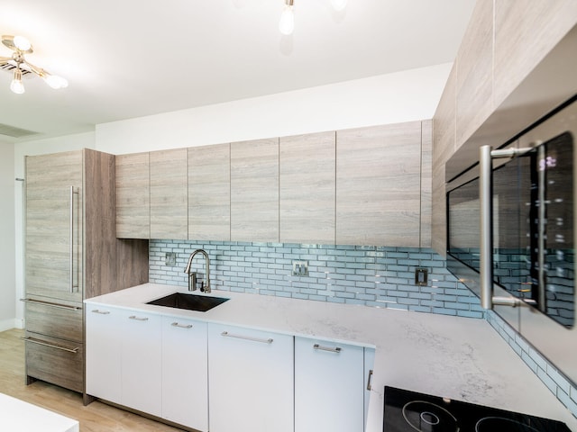 kitchen featuring cooktop, white cabinetry, light wood-type flooring, backsplash, and sink