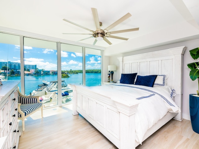 bedroom featuring light wood-type flooring, access to exterior, expansive windows, a water view, and ceiling fan