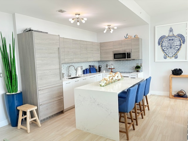 kitchen with a kitchen bar, a center island, sink, tasteful backsplash, and light hardwood / wood-style flooring