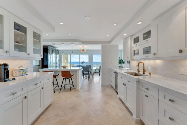 kitchen with decorative backsplash, white cabinets, light stone countertops, a kitchen bar, and sink