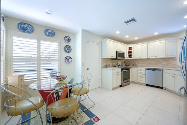 kitchen with appliances with stainless steel finishes, white cabinets, decorative backsplash, and light tile patterned floors