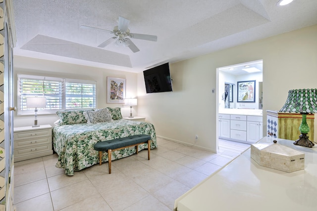 bedroom with a tray ceiling, light tile patterned floors, a textured ceiling, and connected bathroom