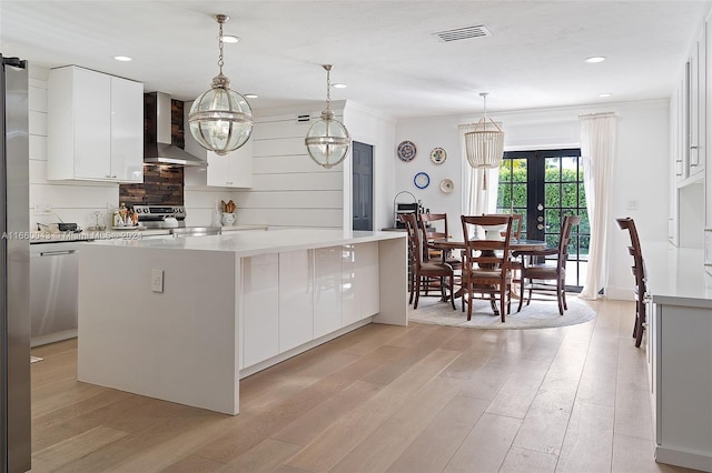 kitchen with a center island with sink, white cabinetry, and wall chimney range hood