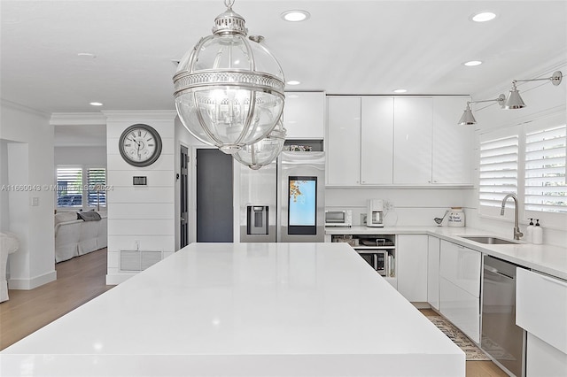 kitchen with white cabinets, light hardwood / wood-style flooring, ornamental molding, sink, and stainless steel appliances