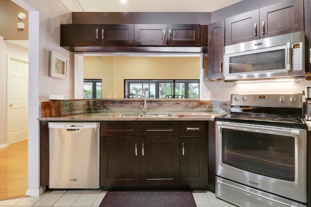 kitchen with appliances with stainless steel finishes, sink, light tile patterned floors, light stone countertops, and dark brown cabinets