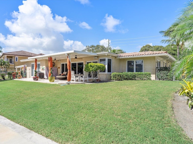 rear view of property featuring ceiling fan, a lawn, and a patio area