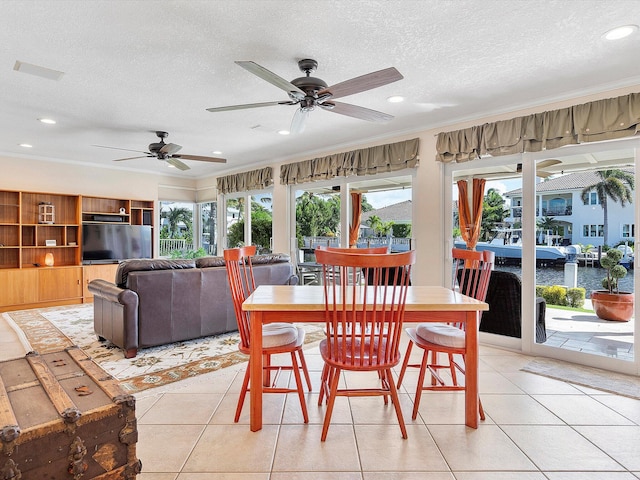 tiled dining area with a textured ceiling, crown molding, a water view, and ceiling fan