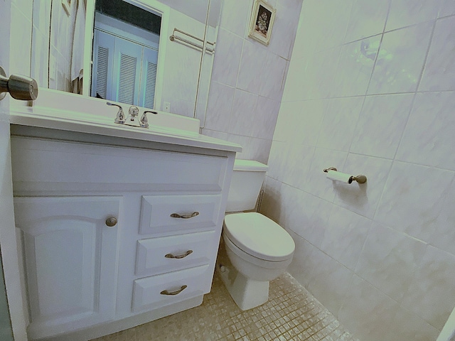 bathroom with toilet, vanity, tile patterned floors, and tile walls