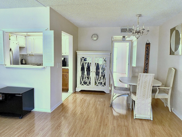 dining area featuring light hardwood / wood-style floors, an inviting chandelier, and a textured ceiling