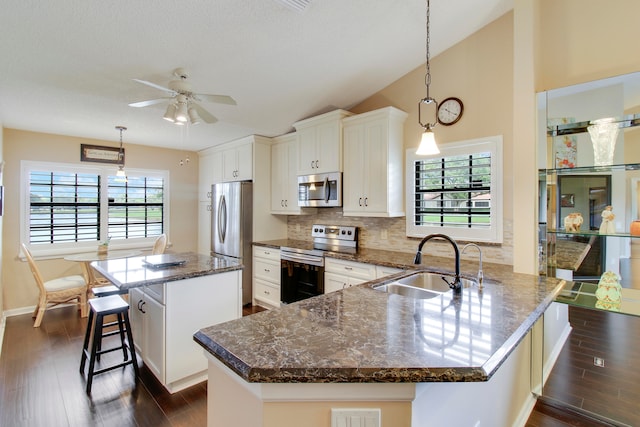 kitchen with stainless steel appliances, sink, kitchen peninsula, decorative light fixtures, and lofted ceiling