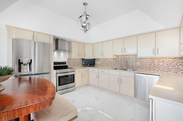 kitchen featuring wall chimney range hood, sink, stainless steel appliances, cream cabinets, and decorative light fixtures