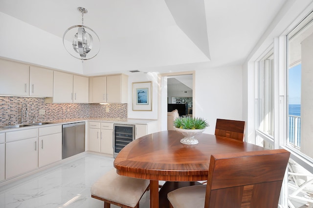 dining space featuring an inviting chandelier, sink, beverage cooler, and a raised ceiling