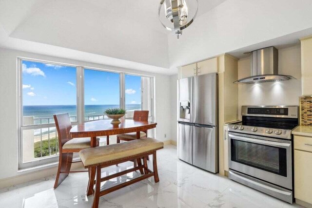 kitchen with a water view, stainless steel appliances, cream cabinets, and wall chimney range hood