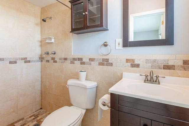 bathroom featuring tile walls, vanity, a tile shower, and toilet