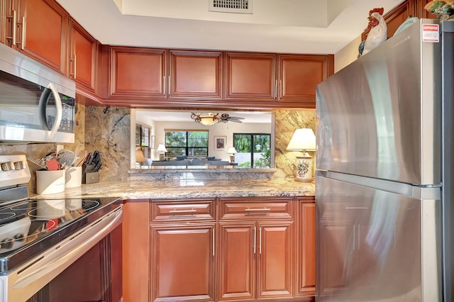 kitchen with light stone countertops, appliances with stainless steel finishes, backsplash, and ceiling fan