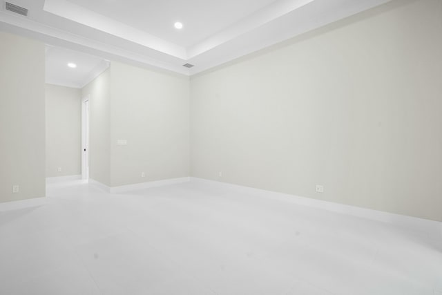 empty room featuring a tray ceiling, crown molding, and tile patterned flooring