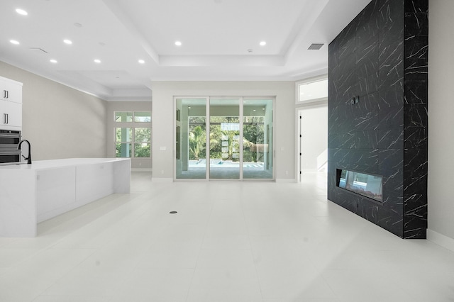 unfurnished living room featuring a raised ceiling, light tile patterned floors, a premium fireplace, and crown molding