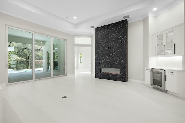 unfurnished living room with a tray ceiling, a premium fireplace, light tile patterned flooring, wine cooler, and bar area