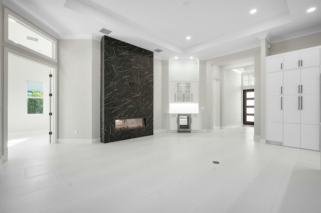 unfurnished living room with beverage cooler, a premium fireplace, ornamental molding, a raised ceiling, and light tile patterned flooring