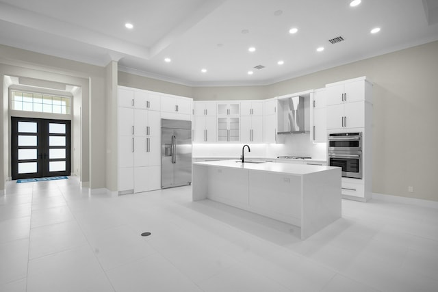 kitchen featuring sink, white cabinetry, a kitchen island with sink, appliances with stainless steel finishes, and wall chimney exhaust hood