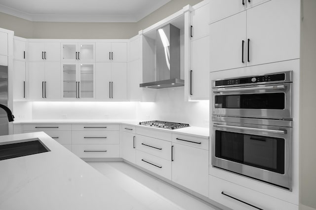 kitchen with wall chimney exhaust hood, crown molding, white cabinetry, and stainless steel appliances