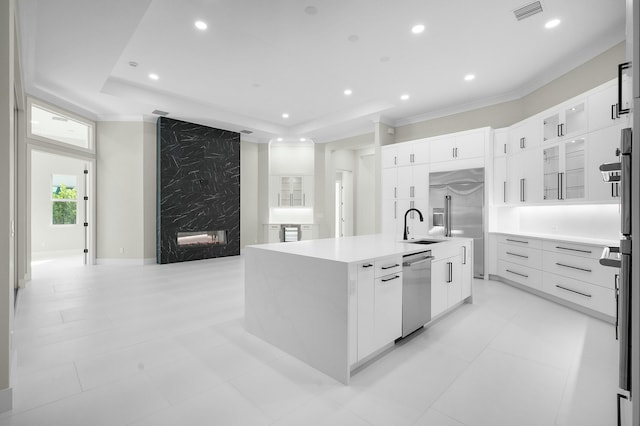 kitchen with a premium fireplace, a tray ceiling, white cabinetry, appliances with stainless steel finishes, and an island with sink