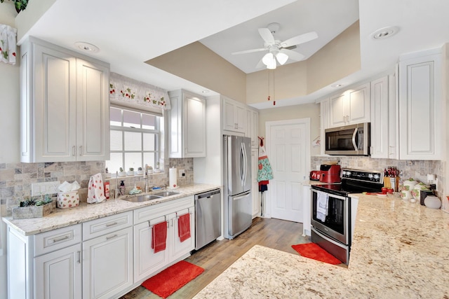 kitchen with appliances with stainless steel finishes, a sink, ceiling fan, light wood finished floors, and backsplash