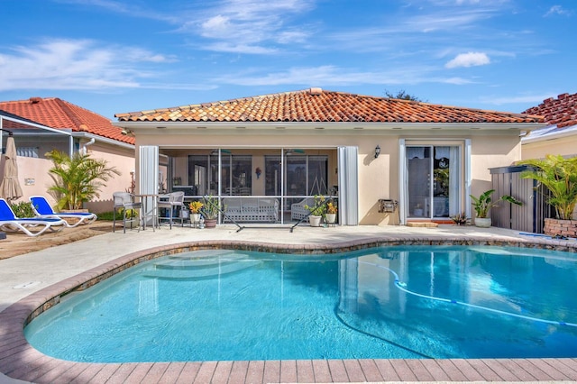 back of property featuring a tiled roof, an outdoor pool, a patio, stucco siding, and a sunroom