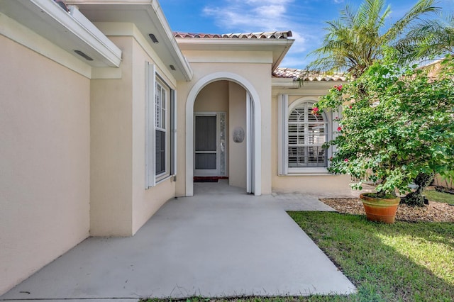 doorway to property featuring stucco siding, a tile roof, and a patio area