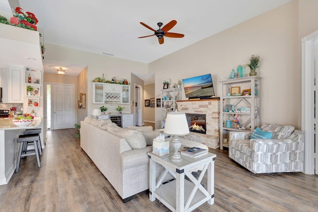 living room with dark wood-type flooring, beverage cooler, a stone fireplace, and ceiling fan