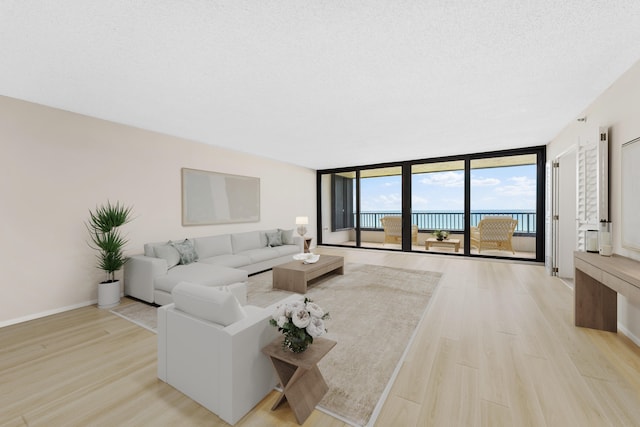 living room with light hardwood / wood-style floors, a water view, a textured ceiling, and floor to ceiling windows