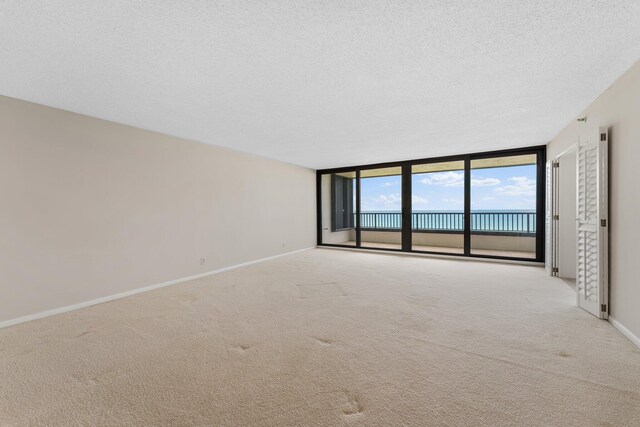 unfurnished room featuring expansive windows, light colored carpet, a textured ceiling, and a water view