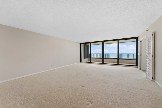 19900 Beach Rd Unit 603, Jupiter, FL 33469 - empty room featuring carpet, baseboards, a wall of windows, a textured ceiling, and a water view
