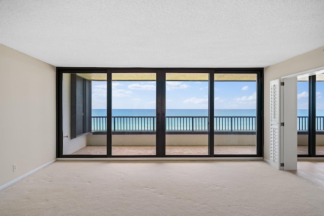 carpeted spare room with a textured ceiling, a water view, and expansive windows