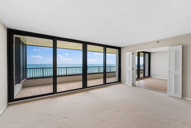 carpeted empty room with expansive windows, a textured ceiling, a healthy amount of sunlight, and a water view