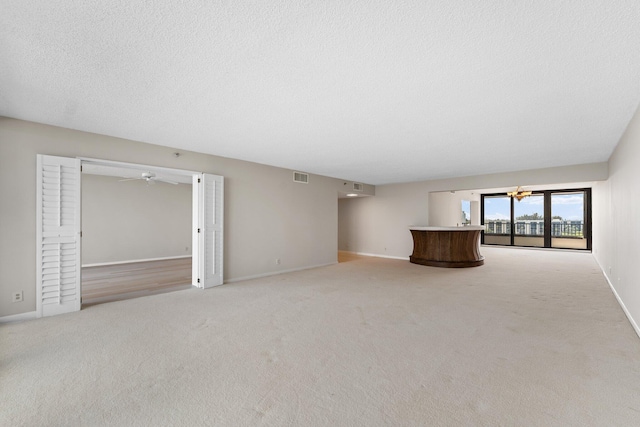 unfurnished living room with light carpet, a textured ceiling, and ceiling fan