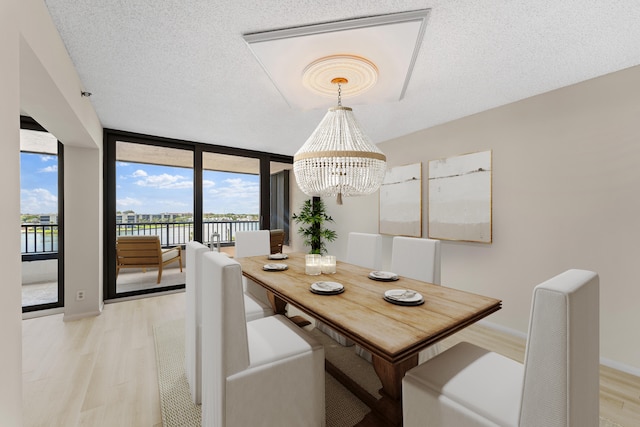 dining area with light hardwood / wood-style floors, a notable chandelier, expansive windows, and a textured ceiling