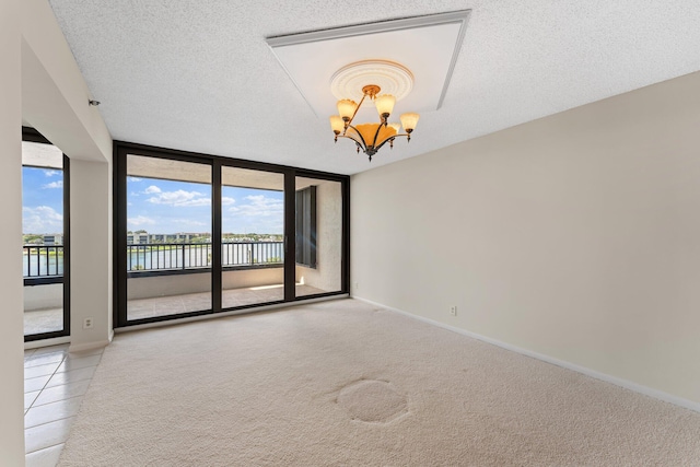 empty room featuring a notable chandelier, light colored carpet, expansive windows, a water view, and a textured ceiling