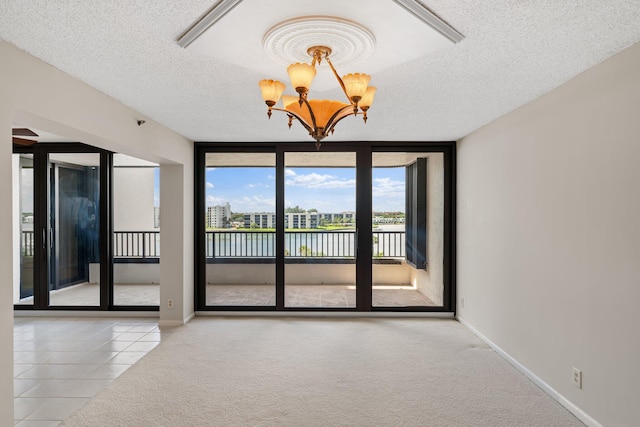 tiled spare room with a textured ceiling, a water view, an inviting chandelier, and floor to ceiling windows